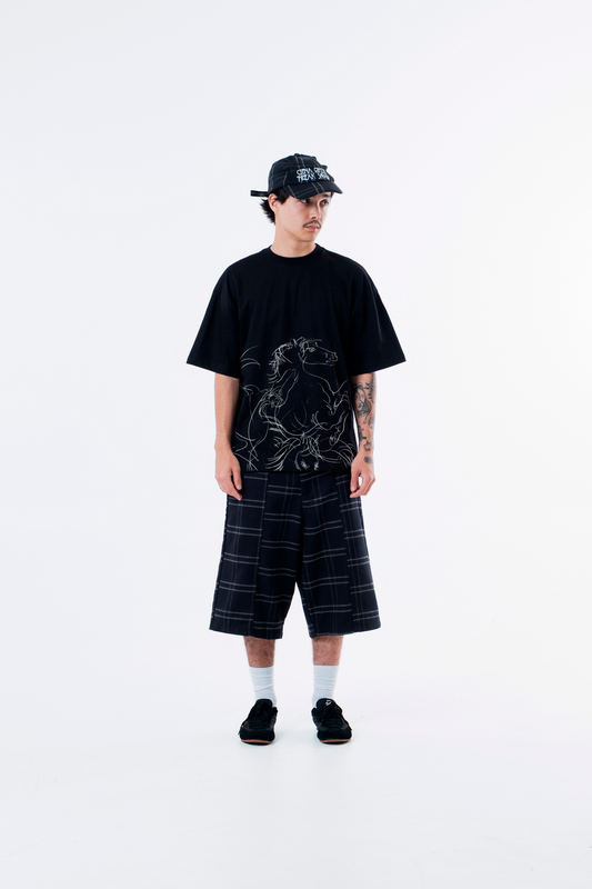 Modelo veste a Cheval Black Heavy Tee preta com bone e bermuda xadrez, vista frontal de corpo inteiro