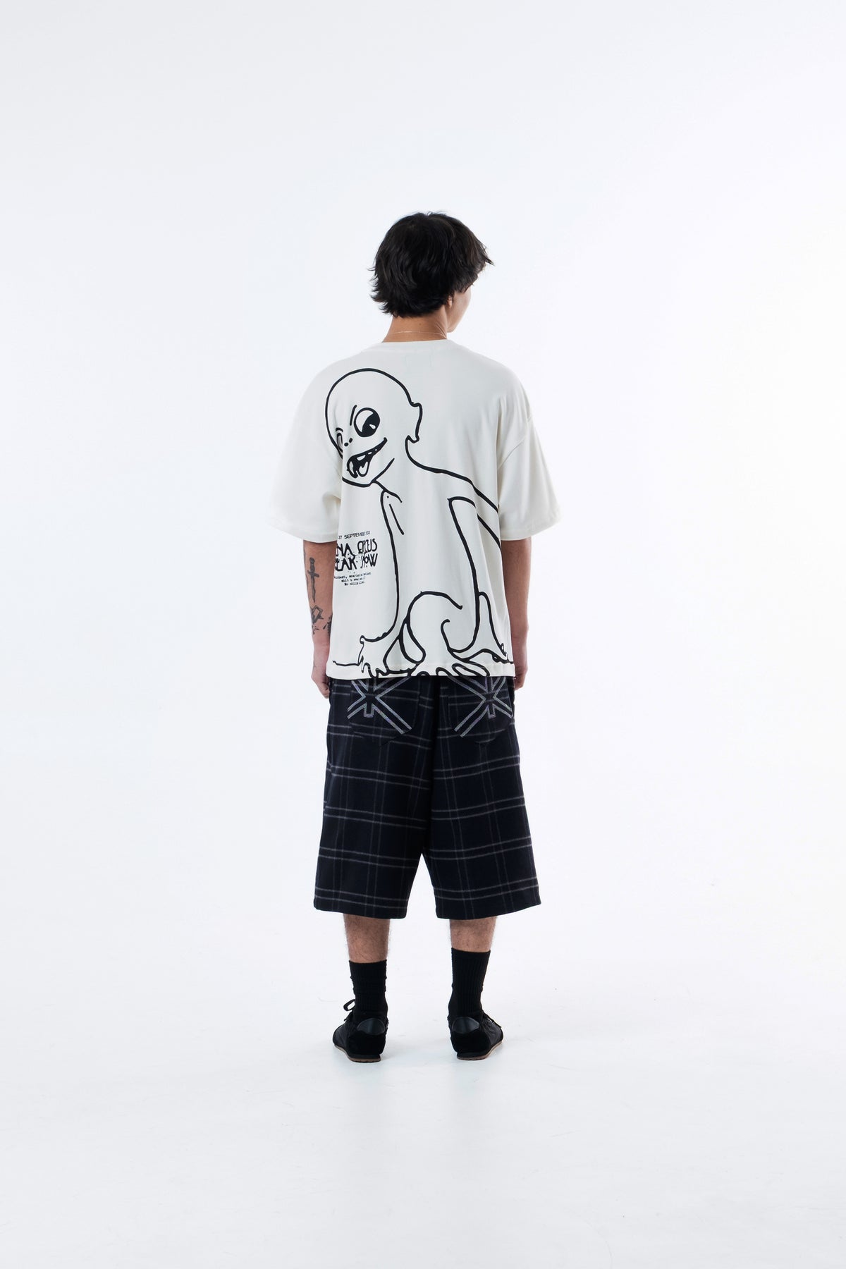 Modelo de costas vestindo a Hypnotist Heavy Tee off-white, com a arte do personagem agachado