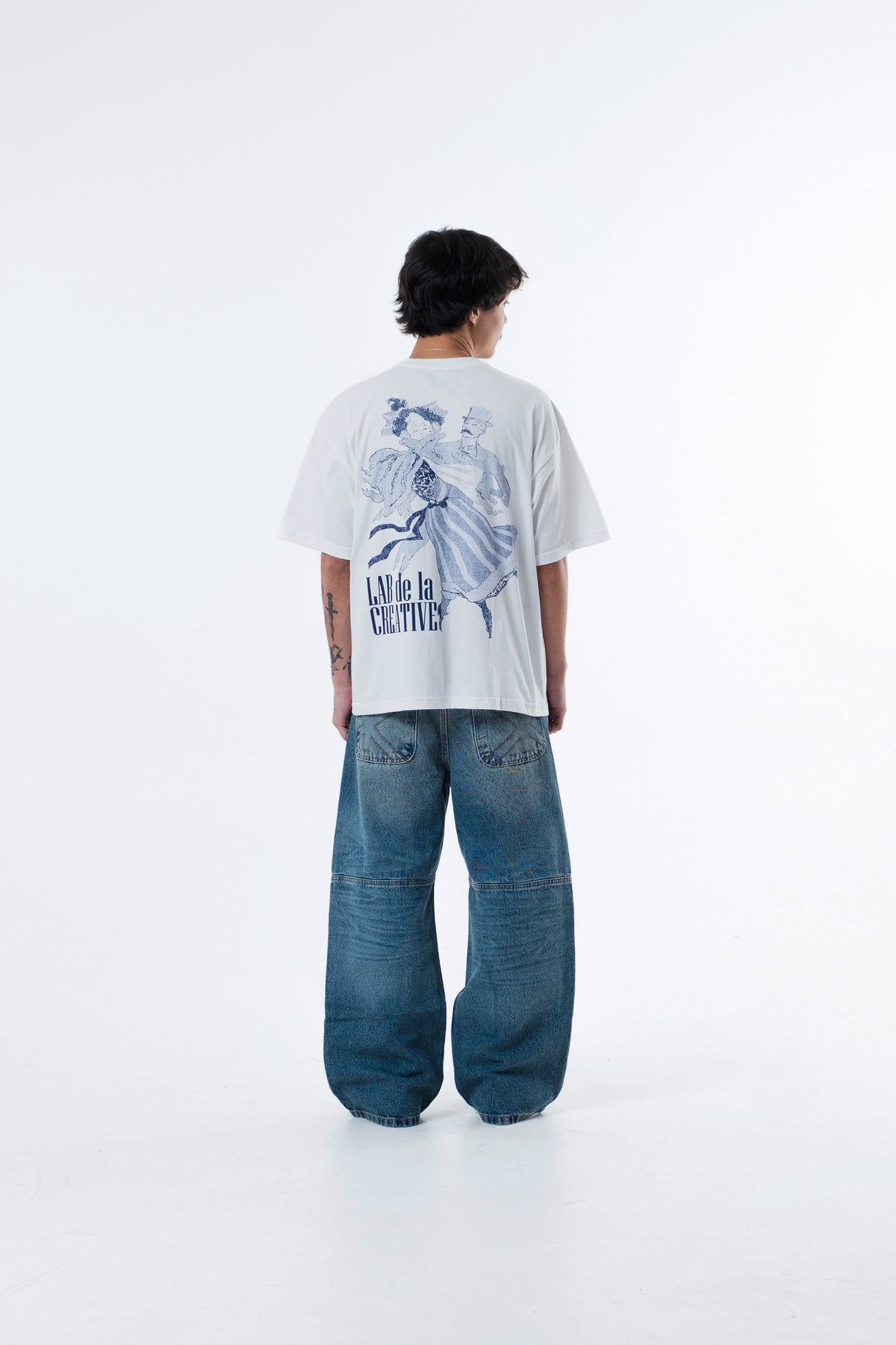 Modelo de costas vestindo a A Danca Classic Tee off-white, com a arte azul do casal dancando