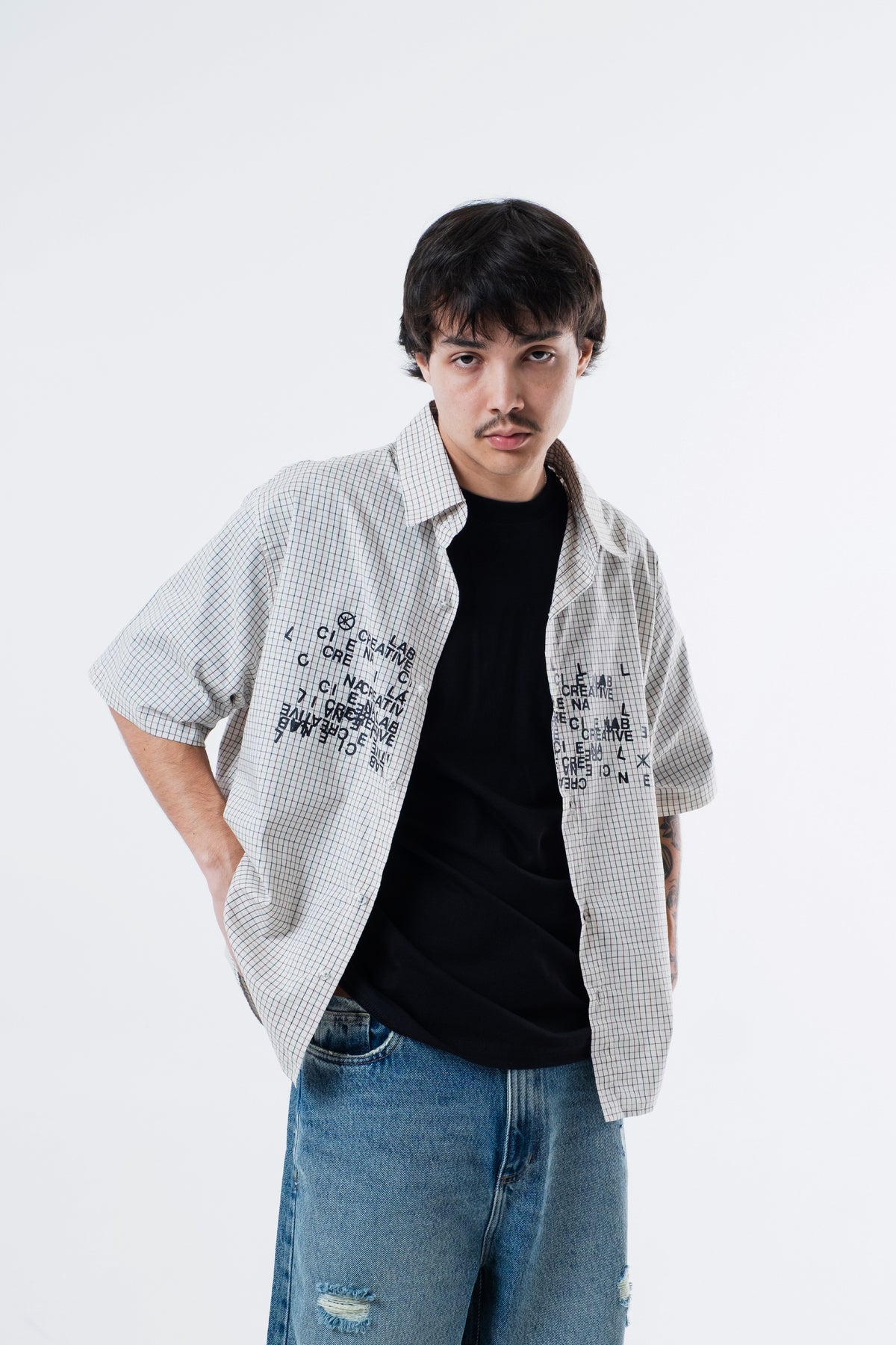 Modelo veste a Xadrez Bege Shirt aberta sobre camiseta preta, enquadramento do tronco