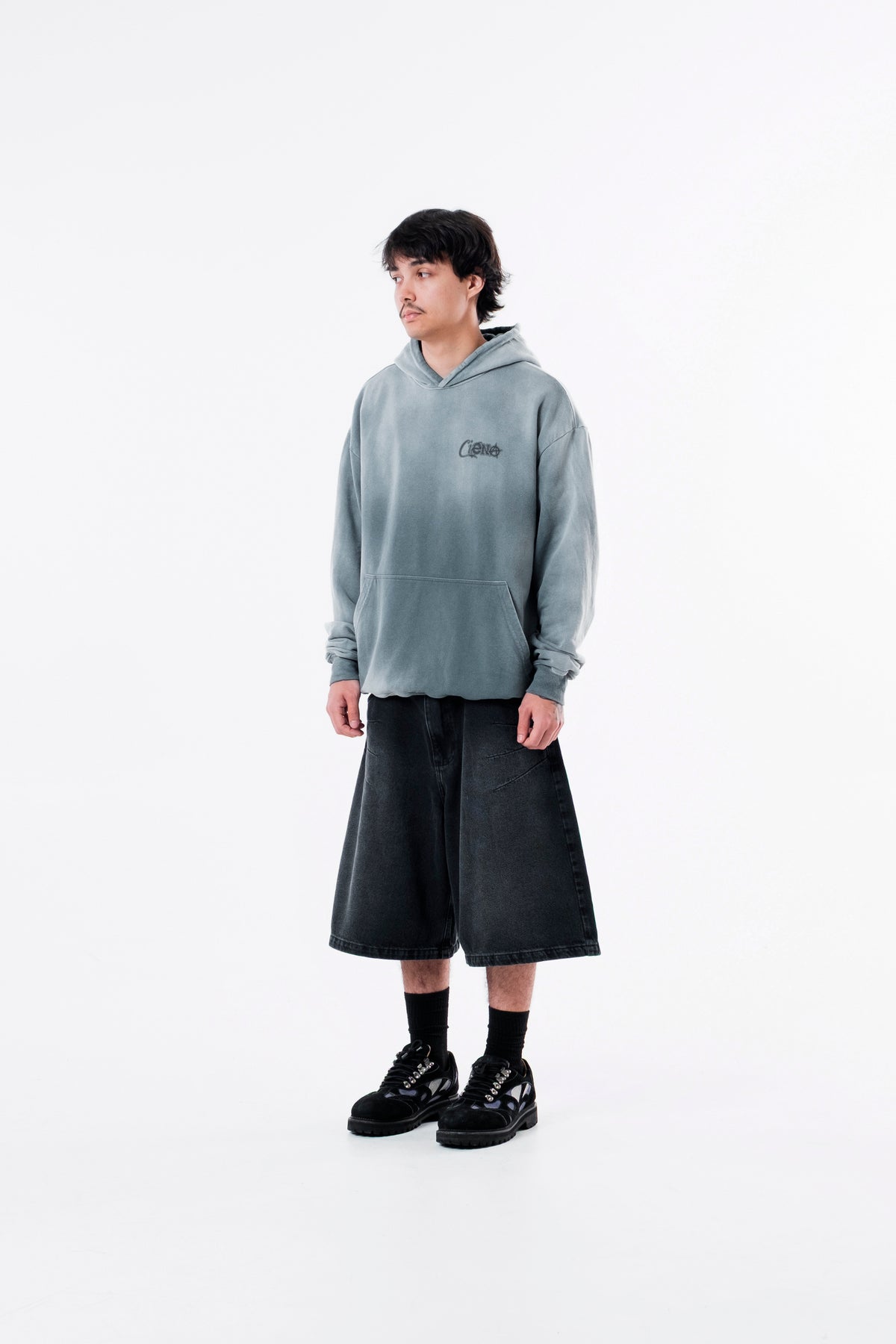 Modelo veste o Aspalth Hoodie cinza com bermuda preta, vista frontal de corpo inteiro