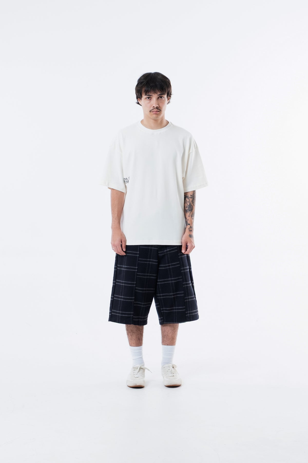 Modelo veste a Mystere Heavy Tee off-white com bermuda xadrez, vista frontal de corpo inteiro