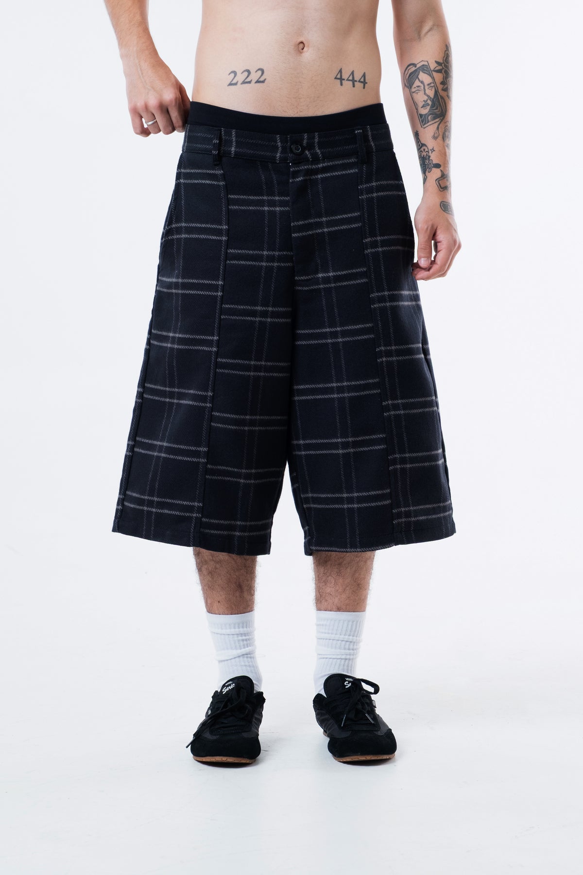 Modelo veste a Xadrez Long Shorts preta, vista frontal do quadril aos pes