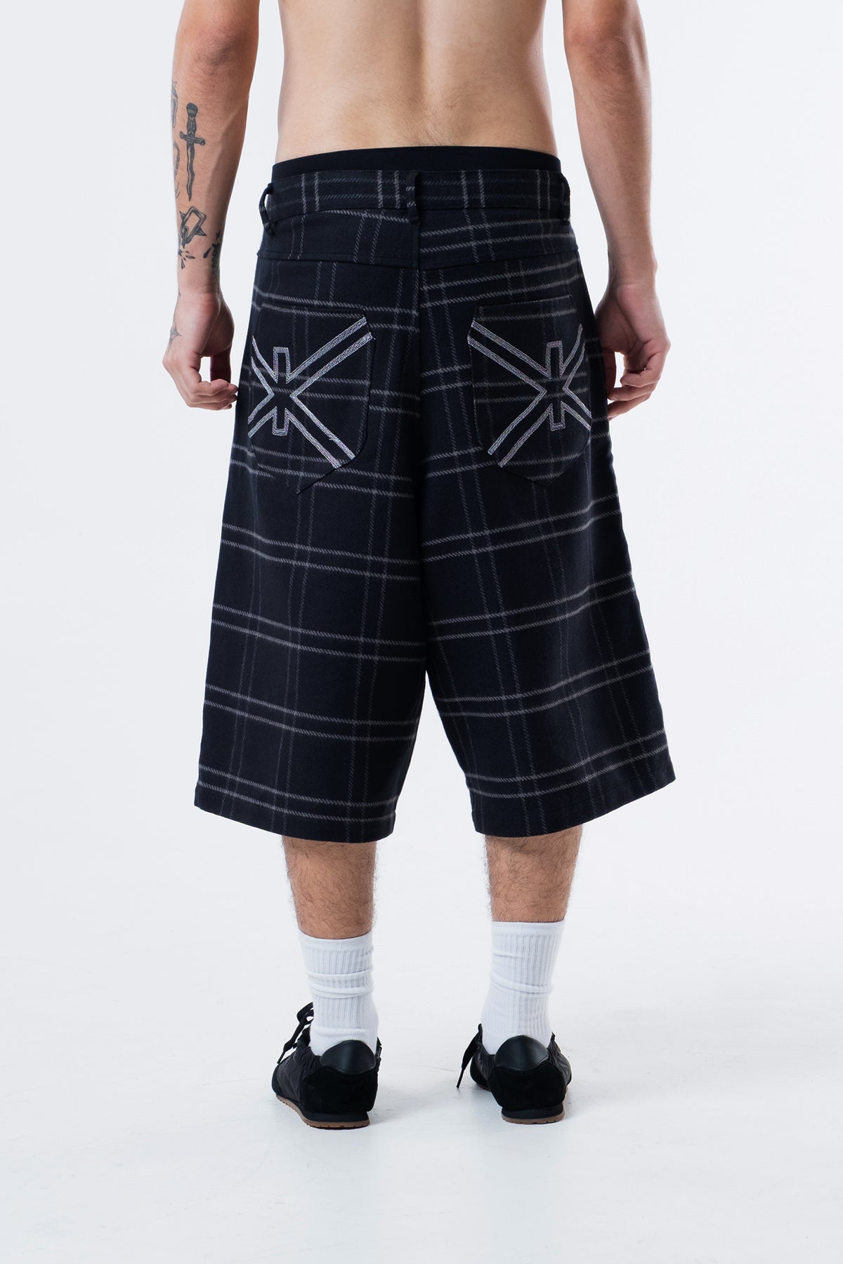 Modelo de costas vestindo a Xadrez Long Shorts preta, com o simbolo Ciena nos bolsos traseiros