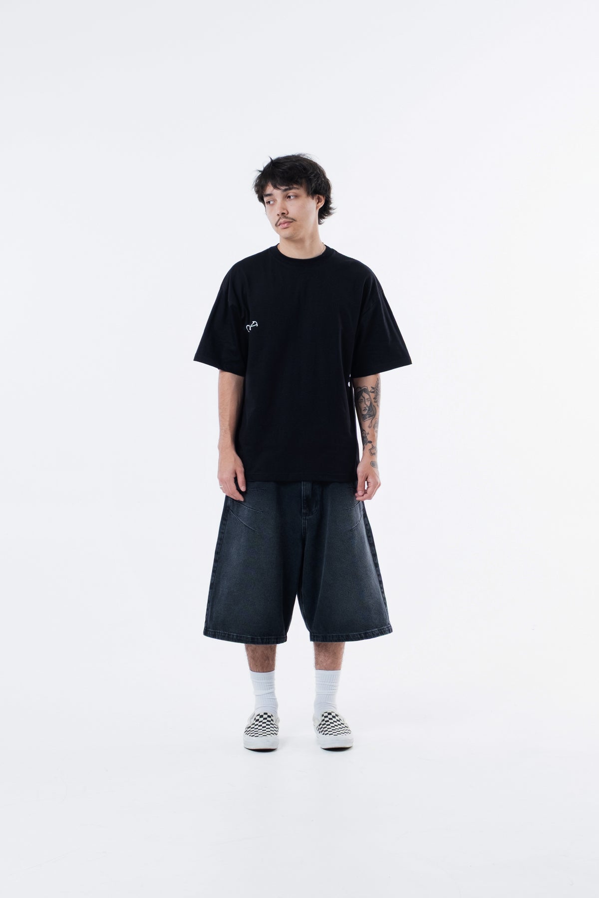 Modelo veste a Joker Figure Classic Tee preta com bermuda preta, vista frontal de corpo inteiro
