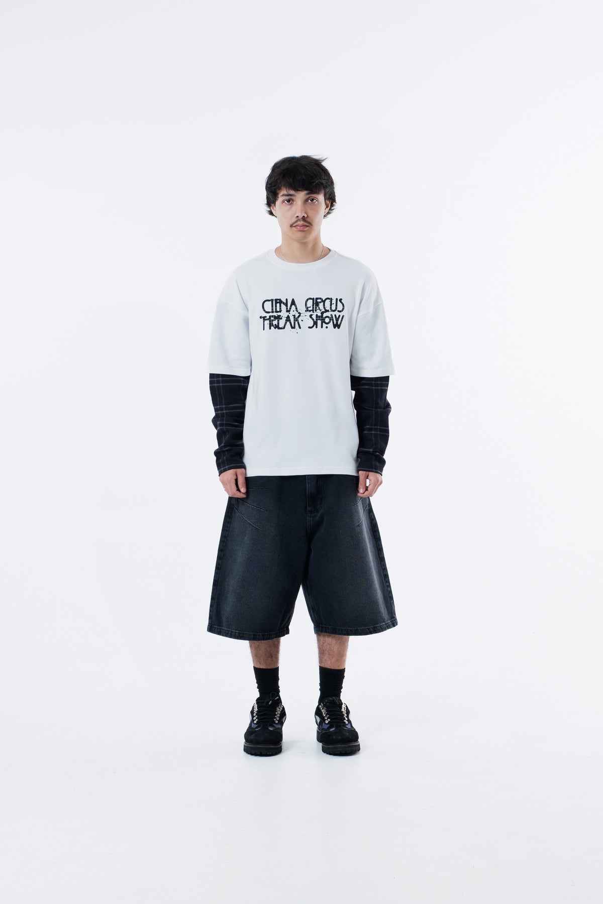 Modelo veste a Freak Show Long Tee off-white com bermuda preta, vista frontal de corpo inteiro