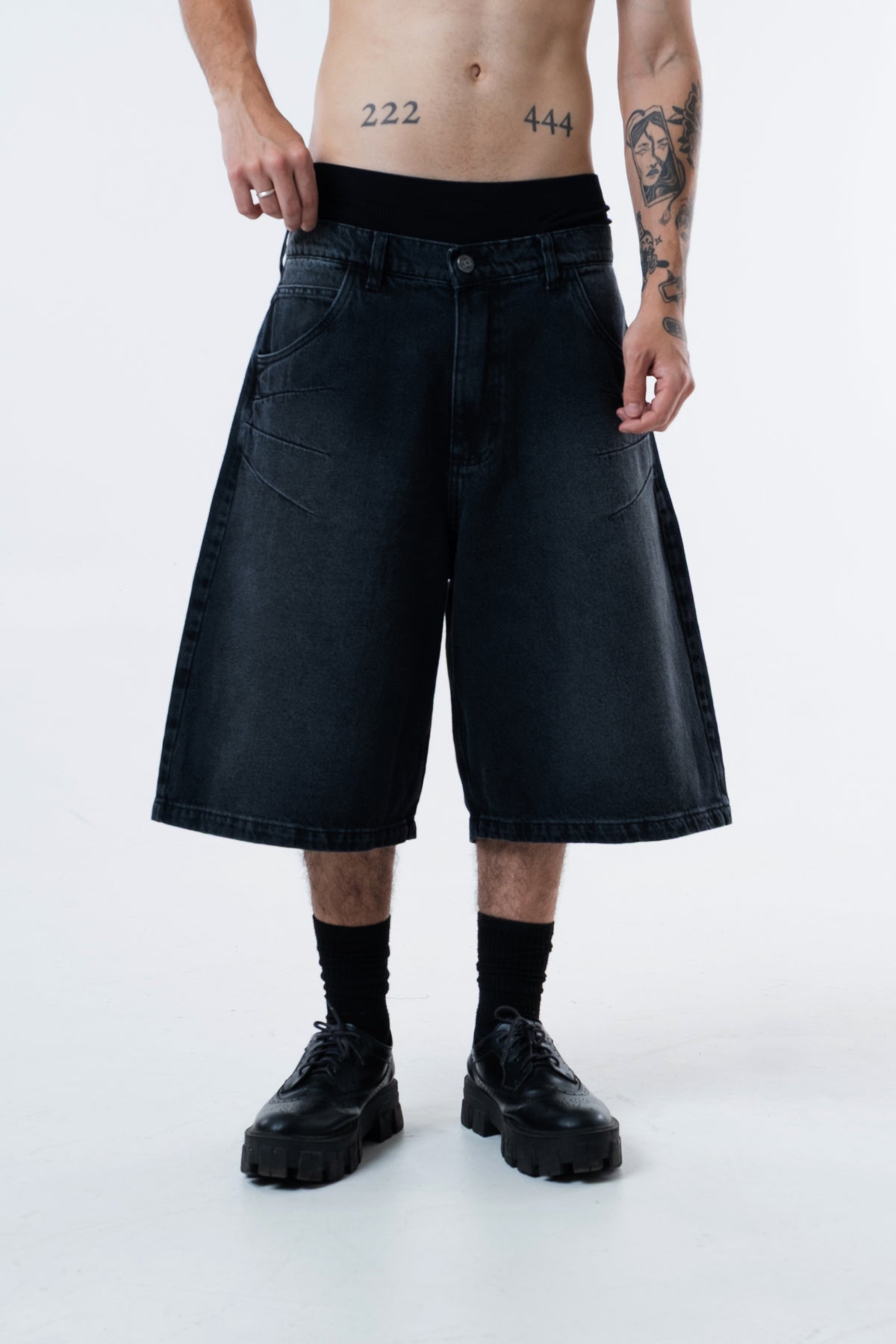 Modelo veste a Asterix Black Jorts preta com bota, vista frontal do quadril aos pes