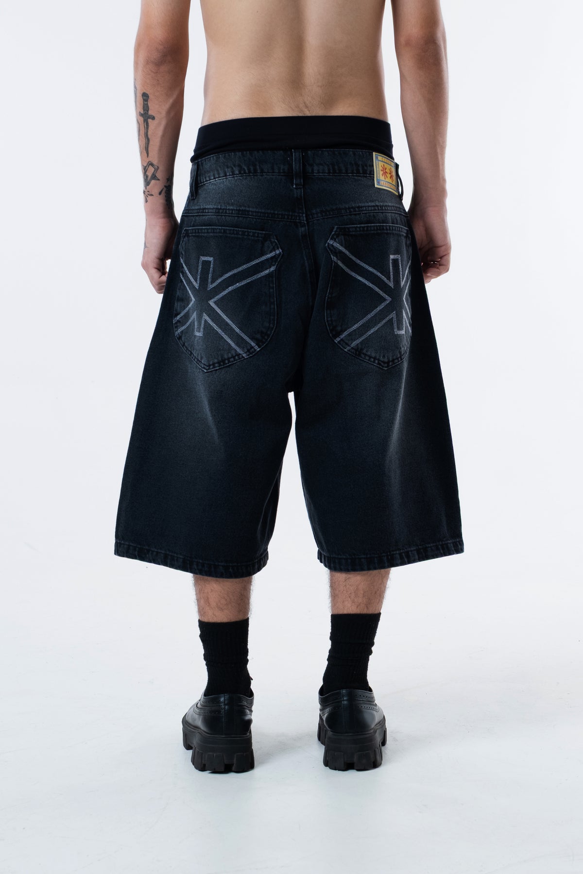 Modelo de costas vestindo a Asterix Black Jorts preta, com o simbolo Ciena nos bolsos traseiros