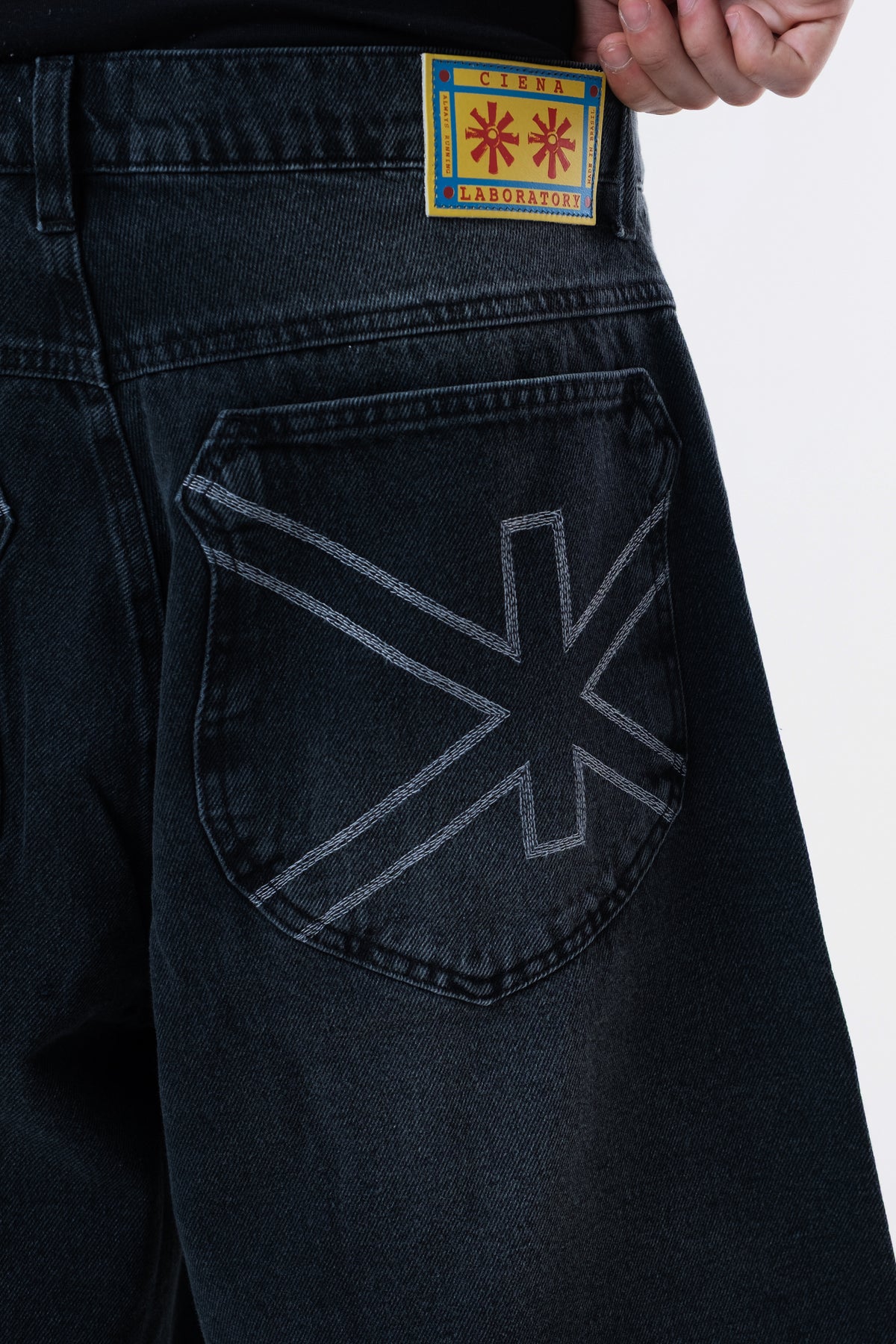 Detalhe do bolso traseiro da Asterix Black Jorts, com o simbolo Ciena costurado e a etiqueta amarela