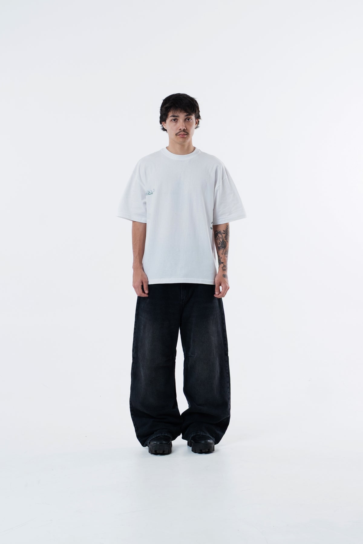 Modelo veste a Triboulet Classic Tee off-white com calca preta ampla, vista frontal de corpo inteiro