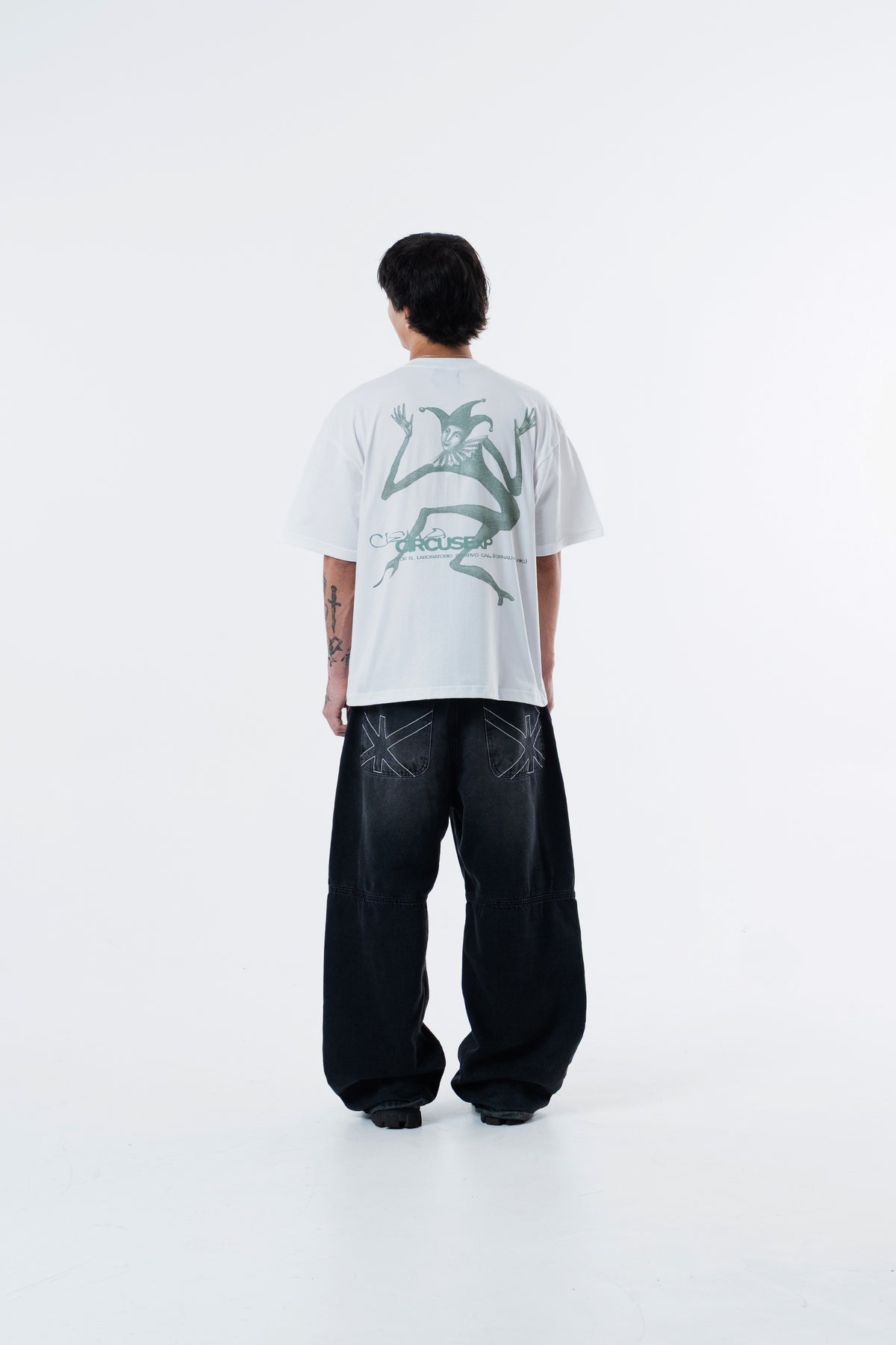 Modelo de costas vestindo a Triboulet Classic Tee off-white, com a arte verde do bobo da corte