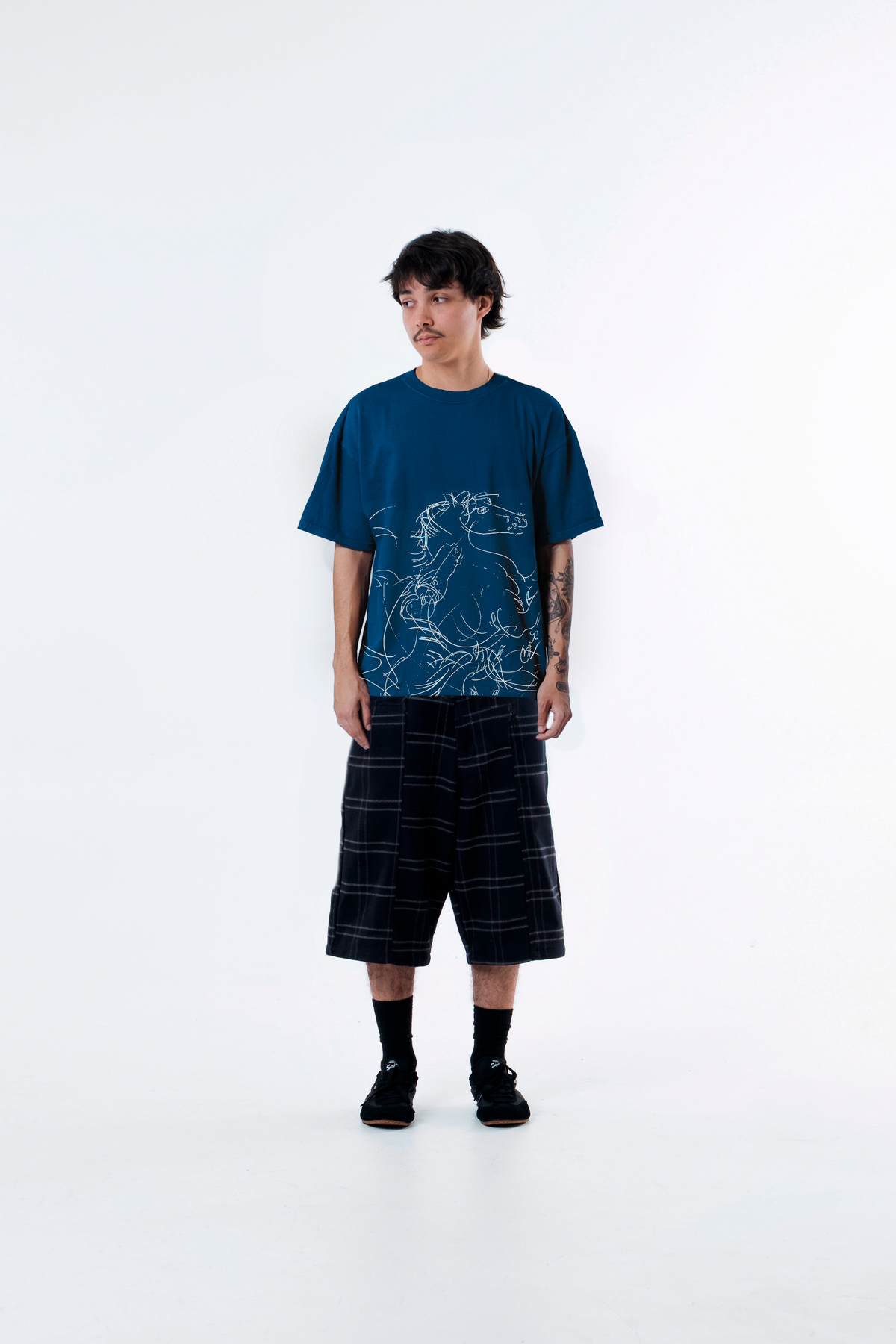 Modelo veste a Cheval Blue Heavy Tee azul com bermuda xadrez, vista frontal de corpo inteiro