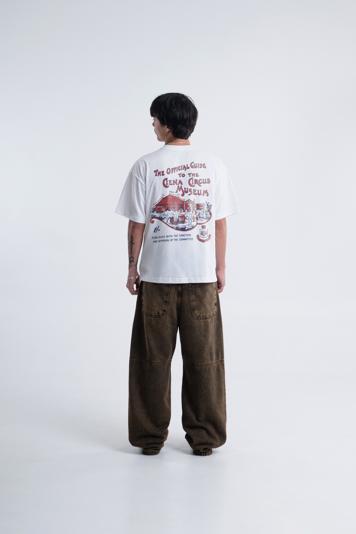 Modelo de costas vestindo a Circus Newspaper Heavy Tee off-white, com a arte do cartaz de circo