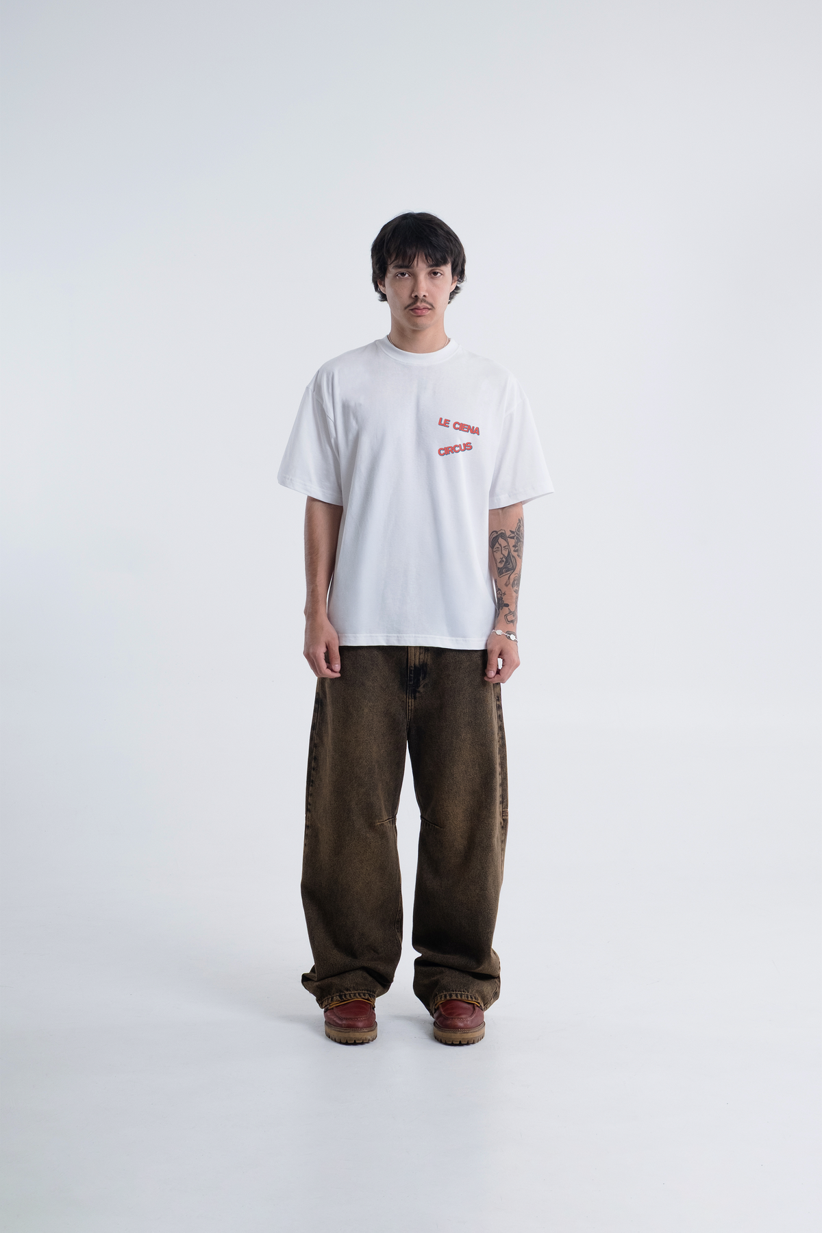 Modelo veste a Circus Newspaper Heavy Tee off-white com calca marrom, vista frontal de corpo inteiro